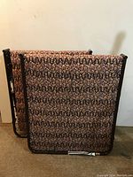 Two folding single cots folded vertically showing patterned foam mattresses and metal frames.