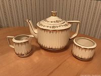 Full tea set including tea pot, creamer, and sugar bowl displayed on wooden table.