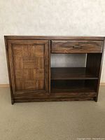 Front view of oak parquet sideboard cabinet showing paneled cupboard door, single drawer with brass handle, and open shelves beneath.