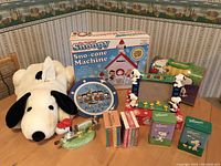 Wide shot showing all items including boxed Snoopy Sno-Cone Machine, Snoopy plush, lunch box, tins, figurines, plate, books, and picture frame