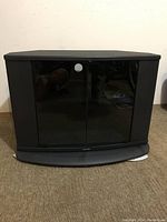 Front view of Toshiba swivel TV stand showing closed smoked glass doors and Toshiba logo on base.