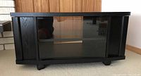 Closed view of black TV stand on rollers with solid side doors and center glass door.