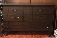 Front view of vintage dark brown plywood dresser showing six drawers and metal hardware, placed on an orange carpet.