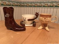 Photo showing three western-themed novelty mugs on a patterned wallpaper background.