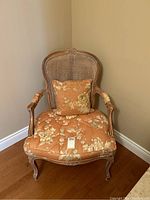 Front view of the antique style cane back armchair showing floral seat cushion and matching pillow.
