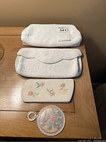 Photo showing all four items: white beaded clutch purse, matching beaded eyeglass sleeve, small beaded floral purse, and compact mirror with floral needlepoint cover.