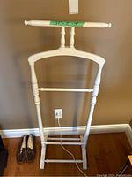 Front view of white painted wooden butler stand with a horizontal bar on top and spindle detailing.