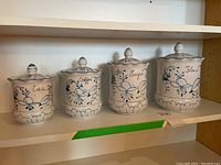 Four ceramic canisters with lids labeled Tea, Coffee, Sugar, Flour featuring hand-painted blue floral patterns.