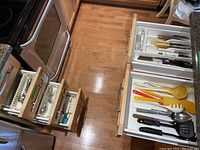 Top view of five kitchen drawers showing different contents including white organizers holding cooking utensils, cutlery trays, and folded tea towels.