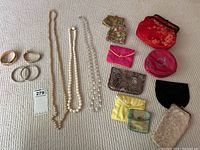 Wide shot showing the four bangle bracelets, three beaded necklaces, and six small cloth travel jewelry purses in assorted colors and styles laid out on a fabric surface.