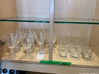 Shelf display of 10 stemware glasses and 8 lowball glasses arranged side by side in cabinet.