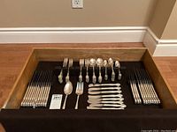 Photo of the entire cutlery set arranged inside a wooden drawer with black felt insert and cloth cover.