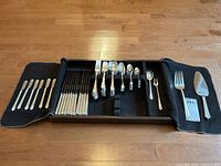 Cutlery set laid out in black sided tray with felt insert and cover, showing various forks, knives, spoons, and serving utensils.
