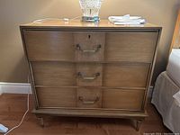 Front view of three-drawer dresser showing overall light oak finish and brass handles