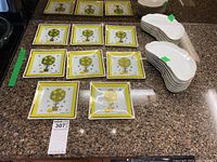 Array of 8 square glass plates with lemon tree design and 13 white ceramic demi lune plates arranged on a countertop.