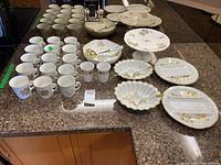 Overview of all hand painted Hammersley china set pieces including mugs, serving platters, divided plates, bowls, and cake plate arranged on counter.