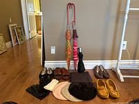 Photo showing umbrellas, shoes in various styles and colors, black and white leather gloves, three wool berets, and a black fringed scarf arranged against a wall on a hardwood floor.