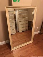 Large framed mirror standing on floor, showing full frame and reflection of furniture.