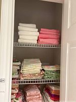Full view of closet shelf with stacked white and coral pink towels on the top shelf and assorted folded sheets below.
