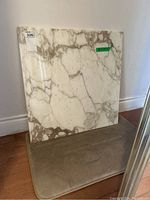 Square marble top slab leaning against a wall, showing natural grey and brown veining on a white polished surface.