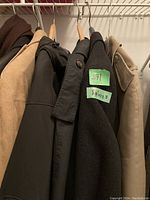 Side view of five men's jackets hanging on wooden hangers including beige, dark brown, black, and gray colored jackets.