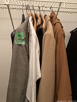Four men's suit jackets and a white dress shirt hanging on hangers in a closet.