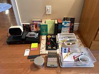Overview of lot items including books, DVD player, alarm clock, stapler, tape dispenser and other desk accessories arranged on a wooden table.