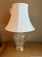 Pair of glass table lamps showing full view with white shades and gold colored bases on wood surface