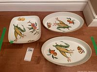 Photo shows three serving dishes: two oval, one square, all decorated with colorful fruit and vegetable designs including corn and peaches. Positioned on wooden floor with lot tag number 356 visible.