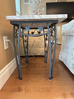 Side view of metal base with decorative leaf and vine design holding the marble top in place.