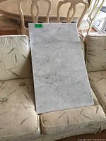 Marble slab resting on beige floral patterned couch showing full length and surface condition.