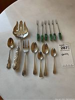 Full view of the complete lot showing 4 Birks sterling spoons, 1 Birks sterling fork, 1 Birks serving fork, 6 Mexican sterling pickle forks with green handles, and 1 additional sterling spoon.
