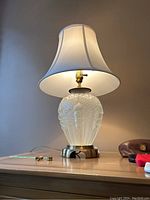 Full view of the lamp showing the frosted glass base with art deco pattern, metal base, and white shade illuminated.