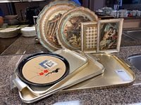 Stack of three metal trays on a countertop showing two round trays with Asian prints and one larger rectangular tray underneath