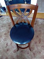 Top view of wooden swivel bar stool showing black vinyl round seat and decorative wooden backrest with X design.