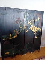 Front view of Japanese four-panel lacquered folding screen with painted figures and architectural scene in muted colors on black background.
