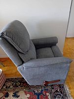 Gray fabric recliner chair in upright position showing side profile with wooden recline lever and cushioned armrests.