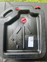 Top view of black plastic drain container with red caps, embossed with 16-quart / 15-liter capacity and drainage indications.