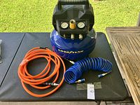 Top-front view of Goodyear air compressor with orange and blue hoses on table outdoors.