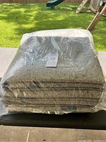 Stack of 6 gray moving blankets wrapped in clear plastic outdoors on a table.