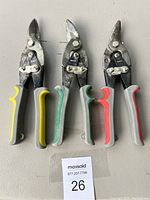 Three metal cutting snips from above showing blades and handles in yellow, green, and red-gray color variations.