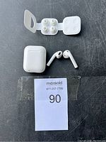 Apple AirPods earbuds, charging case and extra ear tips arranged on a surface with lot label.