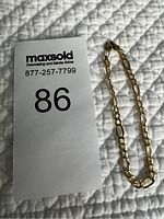 Photo of the gold Figaro link bracelet laid flat on a quilted surface next to a MaxSold number card.