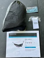 Photo of Basecamp Travel Hammock packed in its black and gray carrying bag alongside a hardware pack and product information sheet.