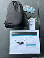 Hammock packed inside black drawstring carry sack, displayed alongside manufacturer tags and listing sheet showing product information and colors.