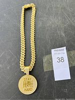 Full view of gold tone chain necklace with round pendant on a black surface.