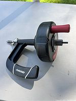 Black Husky brand drain tool with maroon handle and clamp screw, angled view on white background outdoors.