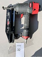 Full side view of Hitachi pneumatic finish nailer with red and black plastic housing and metal nail magazine attached.