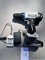 Photo showing HART cordless drill, battery, and charger laid on a surface with clear visibility of model and brand markings