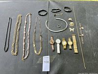 Overview of all jewelry items arranged on a dark surface including necklaces, bracelets, watches, rings, and brooches.